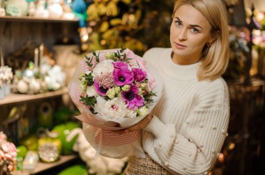 Elinde yeşil yapraklarla süslenmiş pembe ve beyaz şakayık gülleriyle Noel kompozisyonu tutan bir kız.