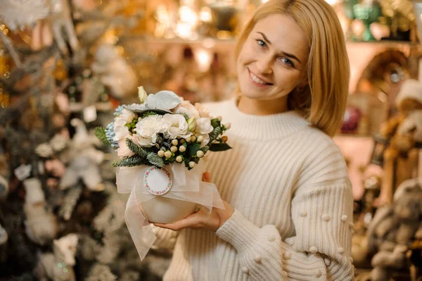 Mujer sosteniendo una maceta con flores blancas decoradas con hojas verdes y ramas de abeto — Foto de Stock