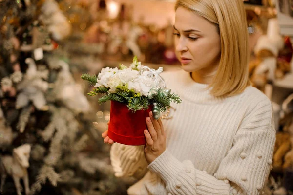 Nő kezében egy piros doboz fehér virágok díszített fenyőfa ágak — Stock Fotó