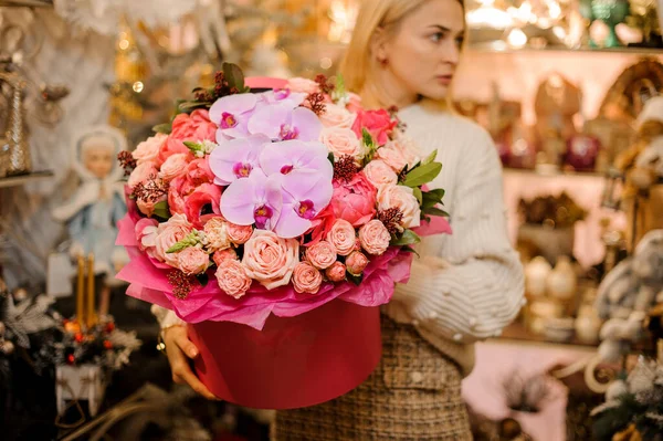 Egy nő kezében egy hatalmas piros doboz őszibarack színű rózsa, világos rózsaszín orchideák és egy másik rózsa színű virágok — Stock Fotó
