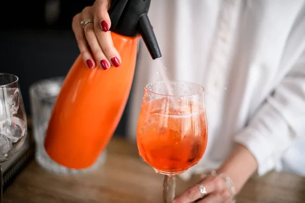 Close-up of glass with orange drink which woman is adding liquid using siphon. — Stok Foto