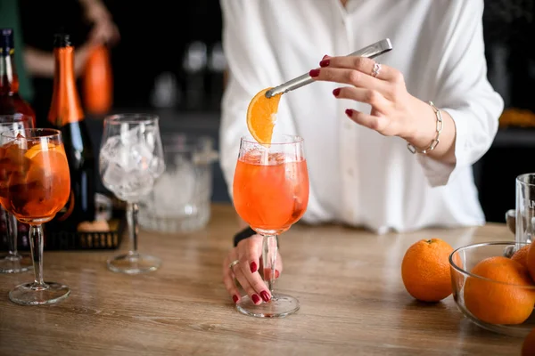 Frau hält Pinzette mit Orangenscheibe über Glas mit Getränk. — Stockfoto