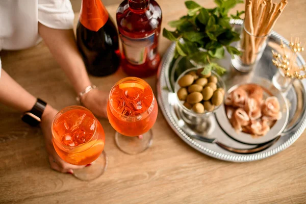มือผู้หญิงถือสองแก้วของเครื่องดื่มสีส้มสดใสเย็นที่ยืนอยู่บนโต๊ะ — ภาพถ่ายสต็อก