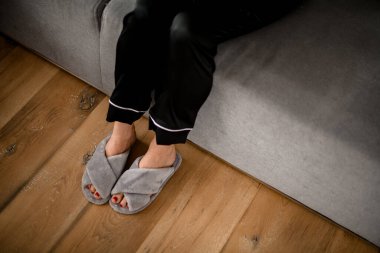 Siyah ipek pijamalı ve gri terlikli bir kadının bacaklarına bakın.