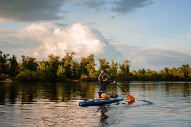 Kadın yemek masasında oturur, kürek çeker ve nehirde yüzer.