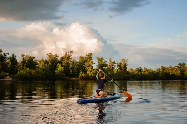 Женщина сидит на доске для ужина держит весло и плавает на реке — стоковое фото