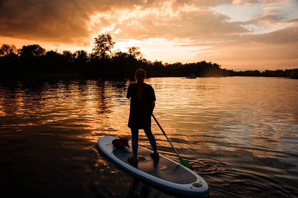 Вид ззаду дівчини на борту, яка плаває на річці на заході сонця — стокове фото