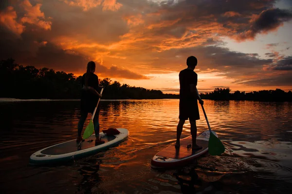 Casal de pessoas em pranchas de jantar no rio ao pôr do sol — Fotografia de Stock