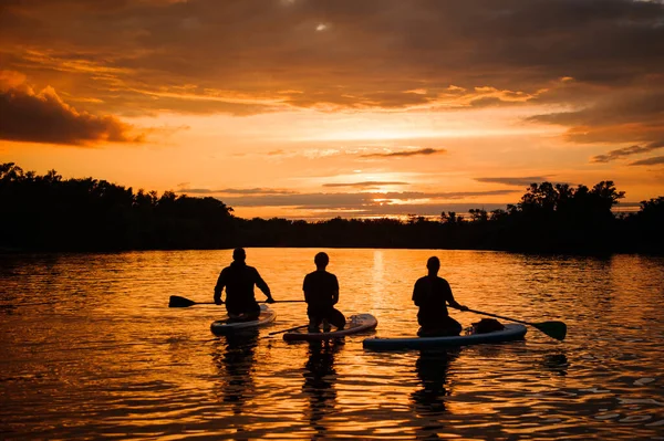 Visszapillantás az emberek sup táblák lapátok úszó a folyón naplementekor. — Stock Fotó
