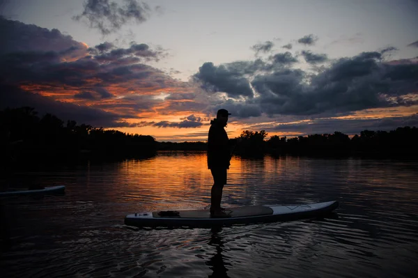 Uomo si erge su tavola di sup sul fiume al tramonto. — Foto Stock