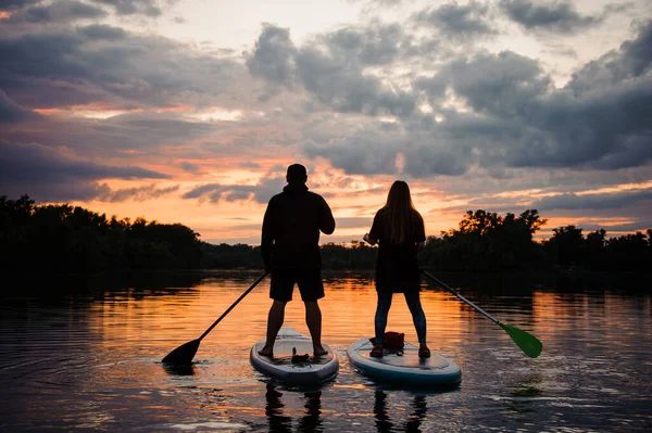 해 가질 때 강에 있는 sup board 위에 있는 두 사람의 뒷모습 — 스톡 사진