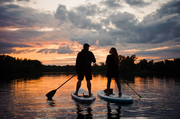 Bella vista posteriore su coppia di persone su tavole di sup sul fiume al tramonto — Foto Stock