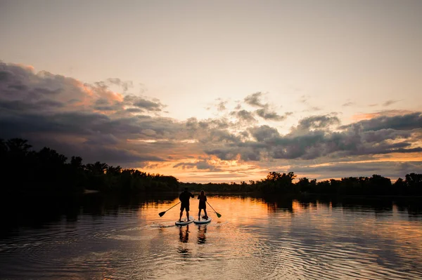 Schöne Aussicht auf Sonnenuntergang und Fluss, auf dem zwei Menschen auf den Surfbrettern schwimmen — Stockfoto