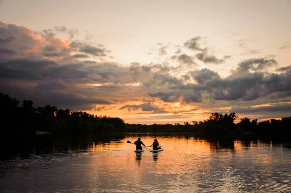 Piękny widok na horyzont i zachód słońca i rzekę, na której para ludzi pływa na deskach — Zdjęcie stockowe