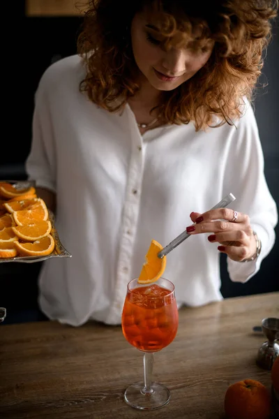 Attraktive Frau hält Pinzette mit Orangenscheibe über Glas mit Getränk. — Stockfoto