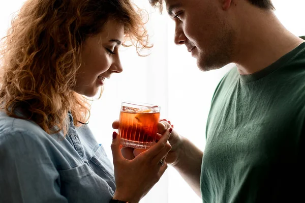 Pria dan wanita tampan berdiri berdekatan dan dengan lembut memegang satu gelas dengan koktail. Stok Gambar Bebas Royalti