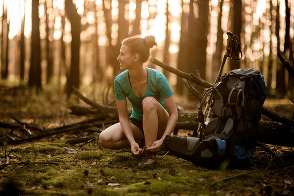 Jeune femme en forêt attache lacets sur les chaussures et regarde loin. — Photo
