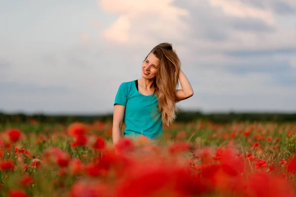 Молода жінка з довгим волоссям, що стоїть на полі з червоними маками . — стокове фото