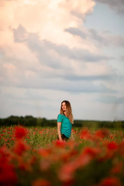 Vista de bela jovem mulher com cabelos longos que de pé no campo com papoilas vermelhas . — Fotografia de Stock