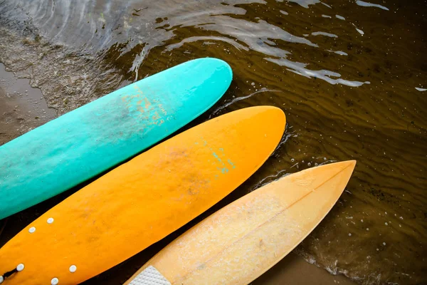 Kilka desek surfingowych leży na brzegu w pobliżu wody. — Zdjęcie stockowe