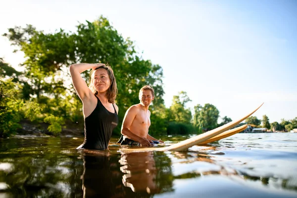 Joven atlético hombre y mujer están sentados en sus tablas de surf en el agua —  Fotos de Stock