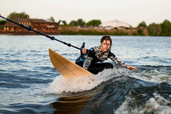 Νεαρή δραστήρια γυναίκα ιππεύει στο wakesurf κρατώντας σχοινί του μηχανοκίνητου σκάφους — Φωτογραφία Αρχείου