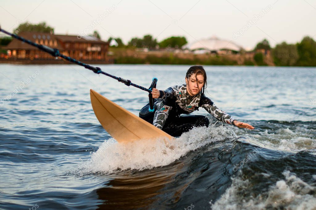 Young active woman riding on the wakesurf holding rope of motorboat