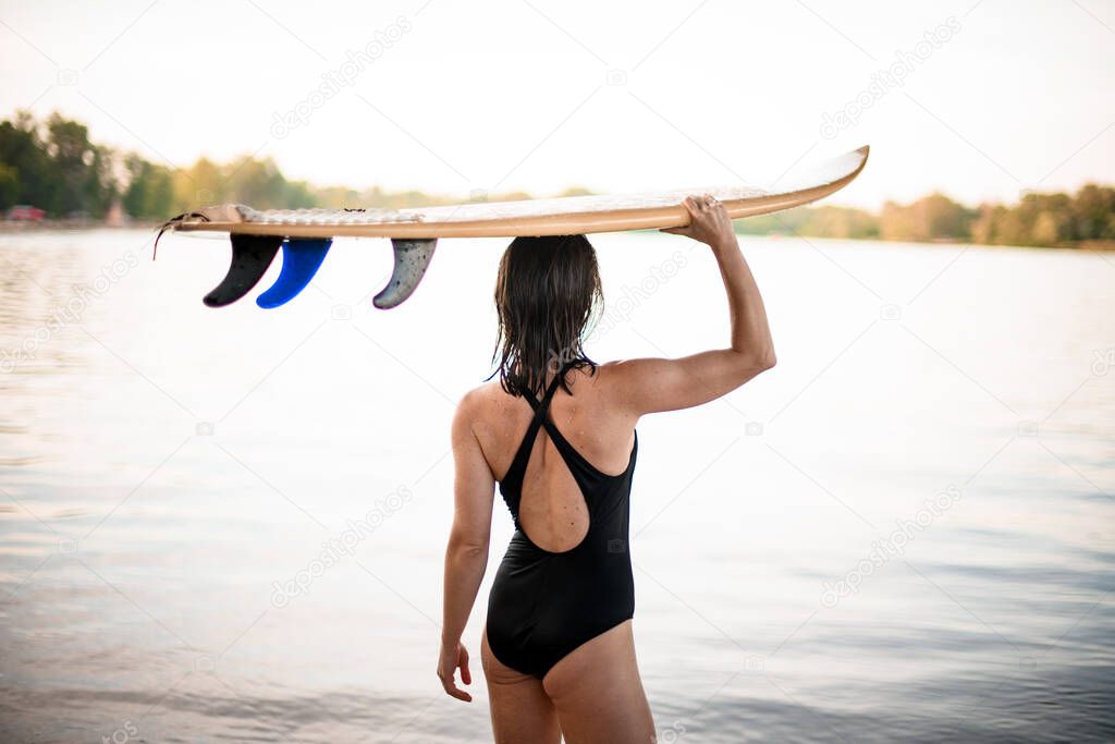 rear view on young athletic woman who carries surfboard on her head.