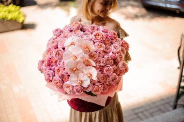 Gülümseyen kadın elinde kocaman bir buket pembe çiçek tutuyor.