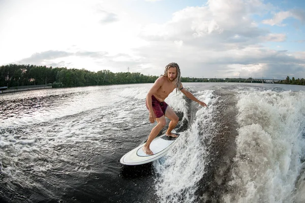 Junger Sportler Wakesurfer mit Dreadlocks reitet auf Surfbrett auf den Wellen. — Stockfoto