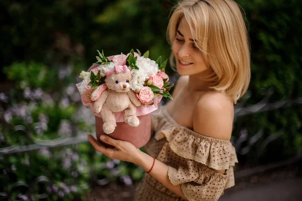 Jeune femme blonde tient boîte ronde mignonne avec des fleurs décorées avec un jouet doux — Photo