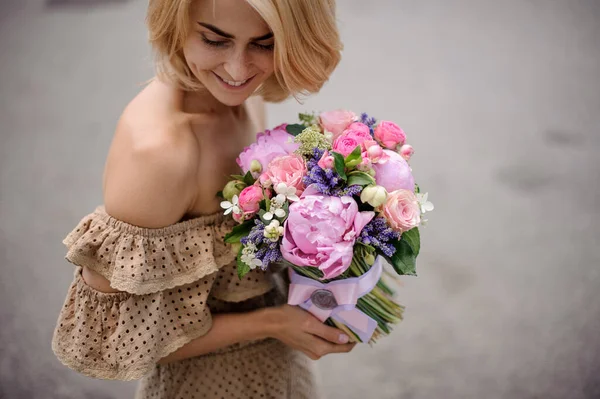 Giovane donna bionda attraente tiene in mano delicato bouquet decorato con nastro di raso — Foto Stock