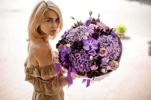Giovane donna bionda con bouquet luminoso di diversi fiori di colore viola — Foto Stock