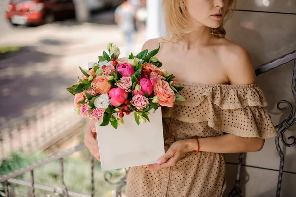 Young woman neatly holds in her hands white square box with flower arrangement — Stock Photo, Image