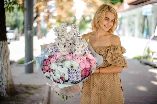 Woman holds in her hand large bouquet of roses, peonies, orchids and white delphinium — Stock Photo, Image