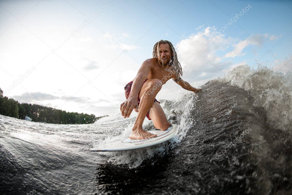 cheerful young man wakesurfing down the river waves