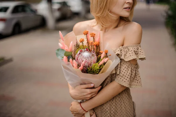 Mujer joven en vestido beige cuidadosamente sostiene en sus manos hermoso ramo de flores exclusivas — Foto de Stock