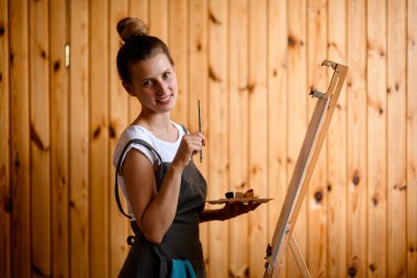 Fırça ve boyalarla gülümseyen kadın ressam kameraya bakar..