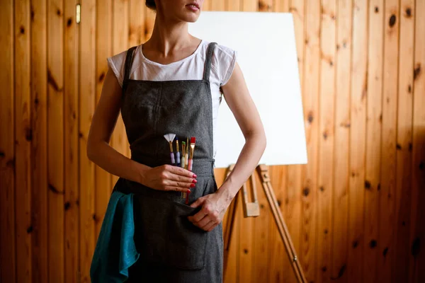 Mujer en delantal gris sostiene varios pinceles en su mano — Foto de Stock