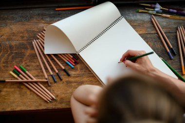 Çizim defterinde renkli kalemlerle resim çizen kadının üst görüntüsü.