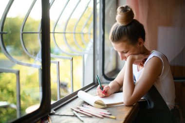 Pencerenin yanında elinde not defteriyle duran ve notlar alan kadına bak