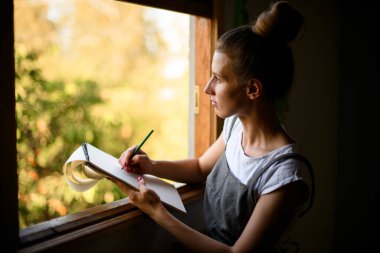 Kağıt defter tutan ve pencerenin yanında not alan kız.