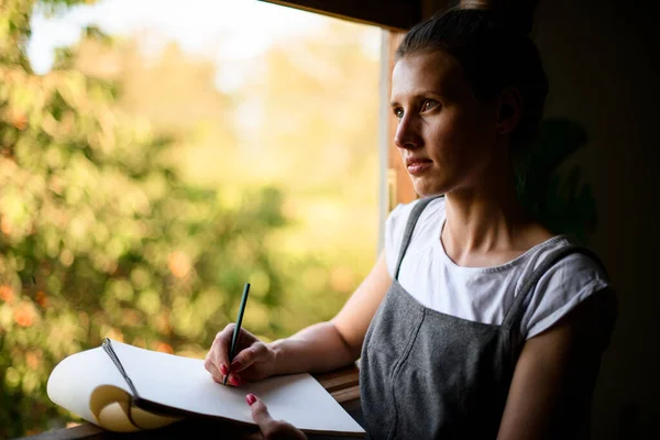 Portrait de belle fille avec cahier en papier qui se tient près de la fenêtre — Photo