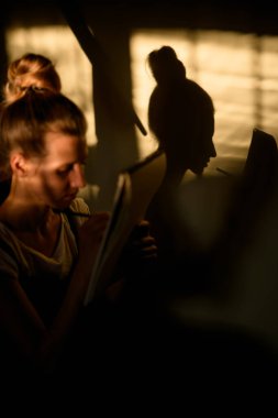 Genç bir kadın oturur ve kafasının gölgesi duvara düşer..