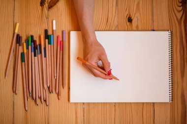 Çizim defterinde çizim yapan kadın elinin üst görünümü.