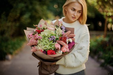 Genç kadın farklı çiçeklerden büyük bir buket tutuyor ve başka tarafa bakıyor..