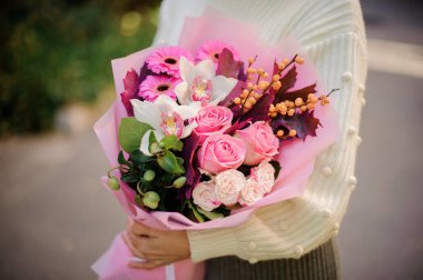 Gül, gerbera, orkide ve böğürtlenli buketin yakın çekimi kadınların elinde..