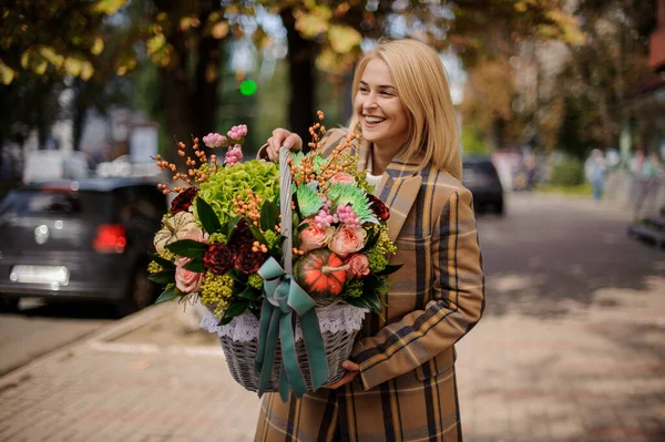 Piękna uśmiechnięta kobieta w płaszczu trzyma kosz z kwiatami wewnątrz. — Zdjęcie stockowe