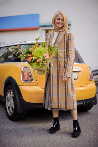 Usmívající se žena v kabátě stojí s květinovým aranžmá v ruce. — Stock fotografie