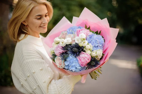 Mujer alegre sostiene ramo de flores blancas, azules y rosadas . — Foto de Stock